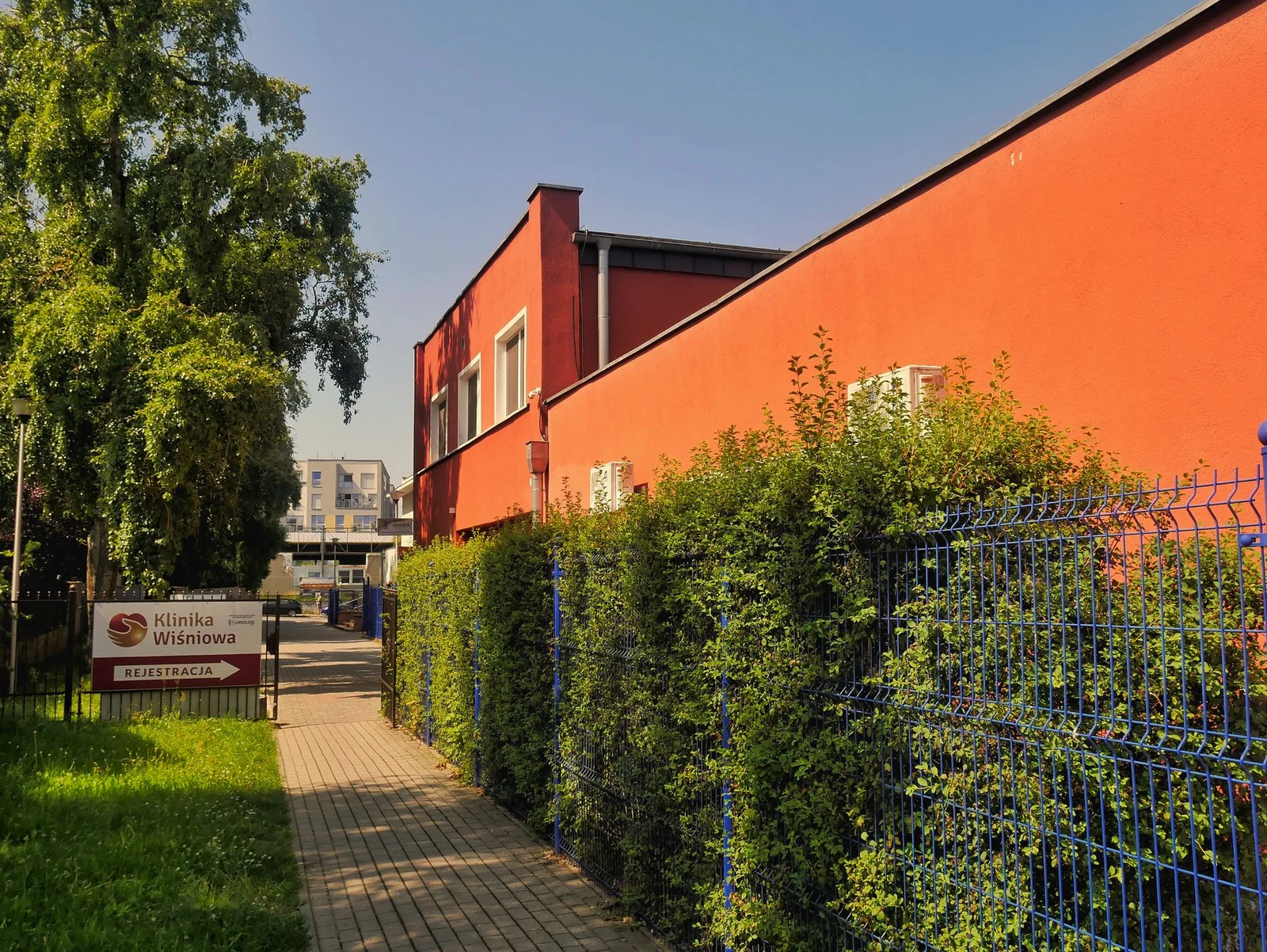 A red clinic building in Poland beside a hedge and fence